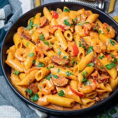 a bowl filled with pasta and meat on top of a blue table cloth next to utensils