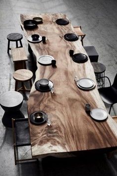 a wooden table with black and white plates on it, surrounded by chairs and stools