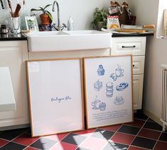 two framed pictures sitting on the floor in front of a kitchen sink and counter top