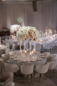 an elegant wedding reception with white flowers and tall centerpieces on round tables surrounded by candles