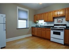 an empty kitchen with wood cabinets and white appliances in the center, along with hardwood floors