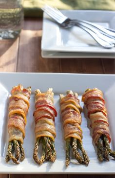 four asparagus wrapped in bacon on a white plate with silverware next to it