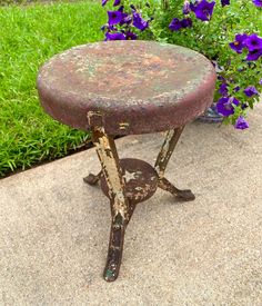 an old stool sitting in front of purple flowers