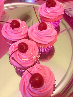 cupcakes with pink frosting and cherries are on a glass platter