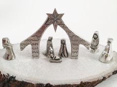 silver nativity figurines sitting on top of a piece of wood in the snow