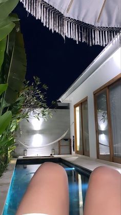 a woman's legs sitting on the edge of a pool in front of a house