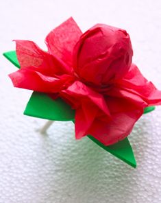 a red flower with green leaves is on a white tablecloth and it appears to be made out of paper