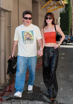 a man and woman walking down the street holding hands with one another, both wearing black leather pants