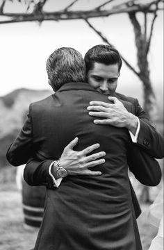 two men hugging each other in front of a tree