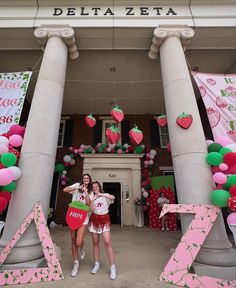 two girls standing in front of a building decorated with pink, green and white balloons