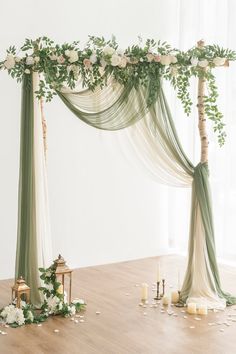 a wedding arch decorated with greenery and white flowers on the floor next to candles