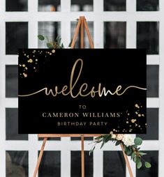 a welcome sign with gold confetti and greenery is displayed on an easel