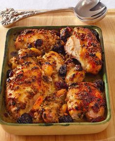 a green casserole dish filled with chicken and fruit next to a silver spoon