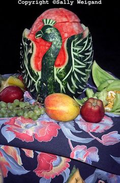 a watermelon carved to look like a peacock surrounded by other fruits and vegetables