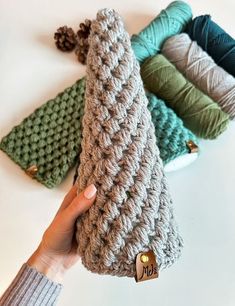 a hand holding up a crochet christmas tree ornament in front of four different colors of yarn