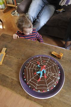 a young boy sitting in front of a spider web cake on top of a wooden table