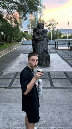 a man standing in front of a statue drinking from a cup