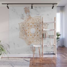 a white and gold wall mural in an empty room with wooden flooring, bookshelf and plant