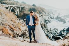 a bride and groom standing on the cliff overlooking the ocean