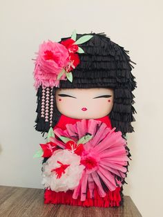 a doll made out of tissue paper with flowers on her head and hair in the shape of a geisha