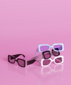 three pairs of sunglasses sitting on top of a pink surface with one pair in the middle