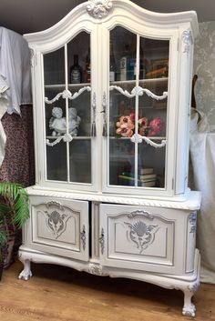 a white china cabinet sitting on top of a hard wood floor next to a potted plant