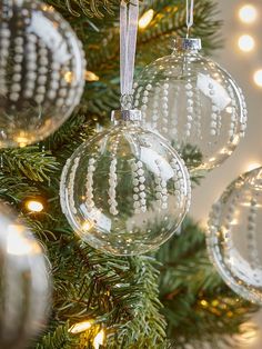 christmas ornaments hanging from a tree with lights in the background