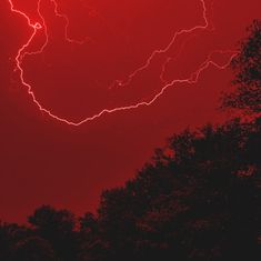 a red sky with lightning striking over trees