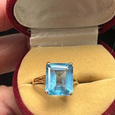 a ring with an aqua blue topazte in a red velvet case, held by someone's hand