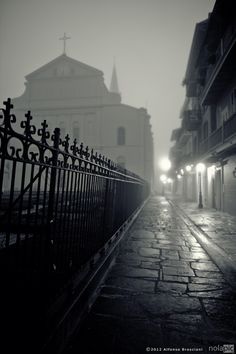 a dark street with an old church in the back ground and light posts on either side