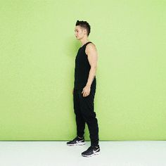 a man standing in front of a green wall with his hands behind his back legs