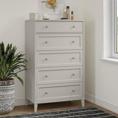 a white chest of drawers next to a potted plant