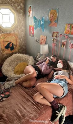 two women laying on a bed in a room with pictures hanging on the wall behind them