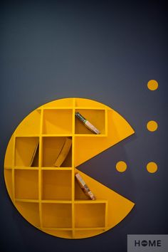 a yellow shelf with some books and pens in it on a blue wall next to circles