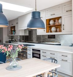 two blue pendant lights hanging over a kitchen island with flowers in a vase on the table