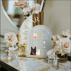 a table topped with vases filled with flowers and glasses next to a sign that says open bar