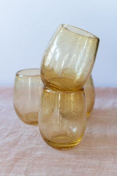 three yellow glasses sitting on top of a pink tablecloth covered table with a white wall behind them