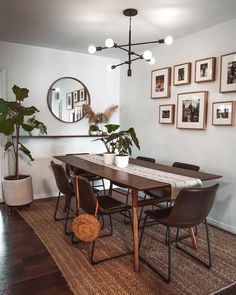 a dining room table with chairs and pictures on the wall behind it, along with potted plants