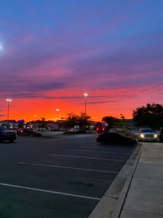 a parking lot with cars parked in it and the sun going down behind the clouds