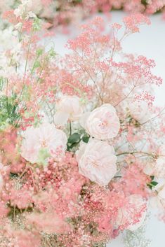 pink and white flowers are in a vase on the table, with greenery around them