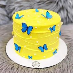 a yellow cake with blue butterflies on it sitting on top of a fur covered table