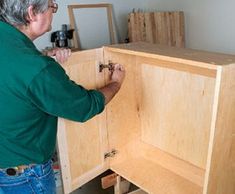 a man in green shirt working on wooden cabinet