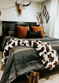 a cow print bed spread and pillows in a bedroom with deer head on the wall