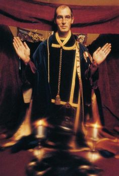 a man in a priest's robe standing with his hands up and two other men behind him