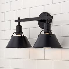 two black lamps are on the wall in front of a white brick wall and light fixture