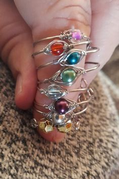 a person's hand holding several rings with different colored stones on them, all in various sizes and shapes