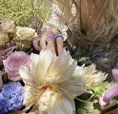 a woman sitting in front of a bunch of flowers with rings on her finger and ring