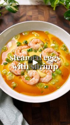 a white bowl filled with soup and shrimp on top of a wooden table next to green leaves