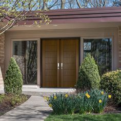 a house with two large wooden doors in front of it and flowers on the side