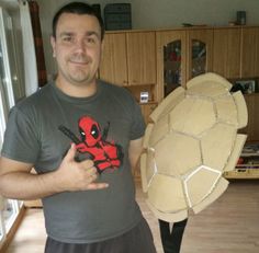 a man is holding a turtle shell and giving the thumbs up while standing in a living room